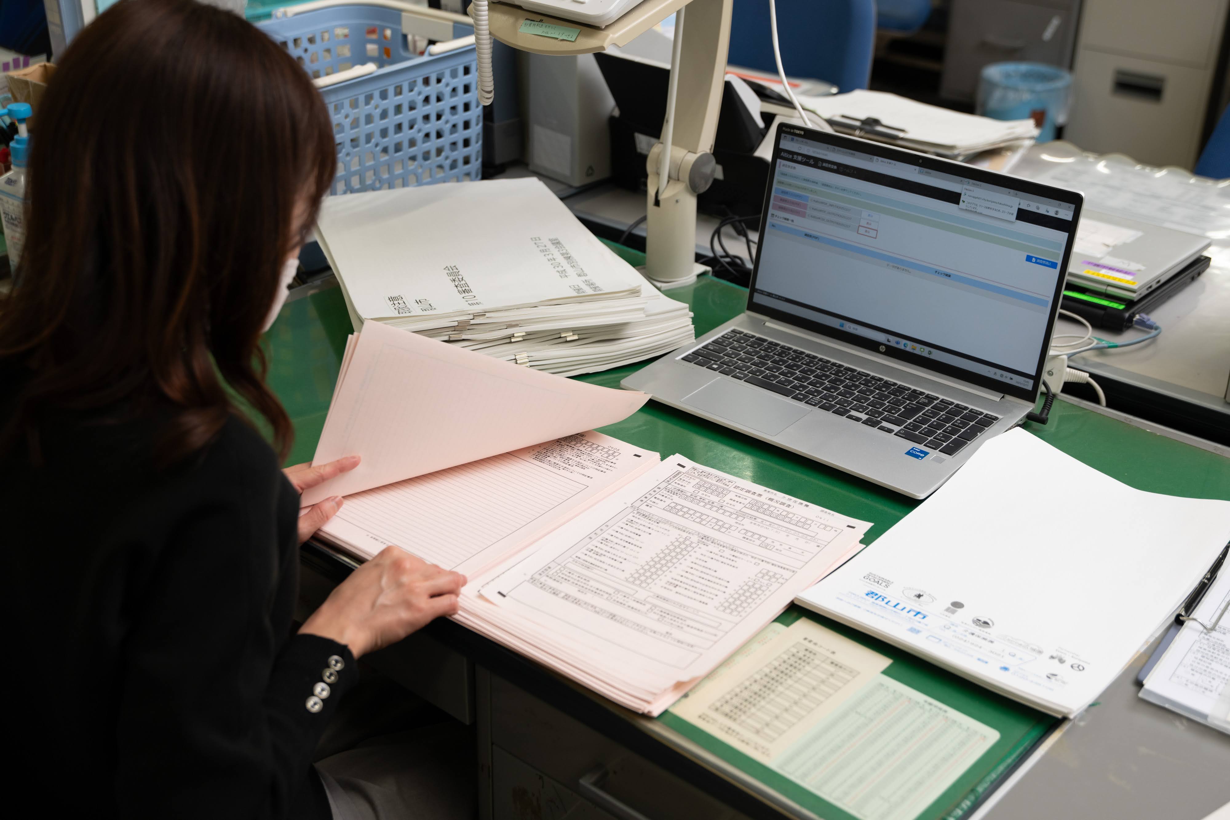 認定調査票の内容を確認する郡山市役所職員の写真。着席している机の上にはノートパソコンが開いてあり、手元には認定調査票が見える。