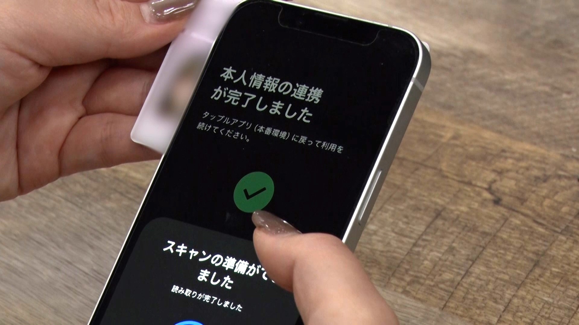 スマートフォンを右手に持ち、左手に持つマイナンバーカードをスマホにかざして、本人認証を行う手元の様子を写した写真。