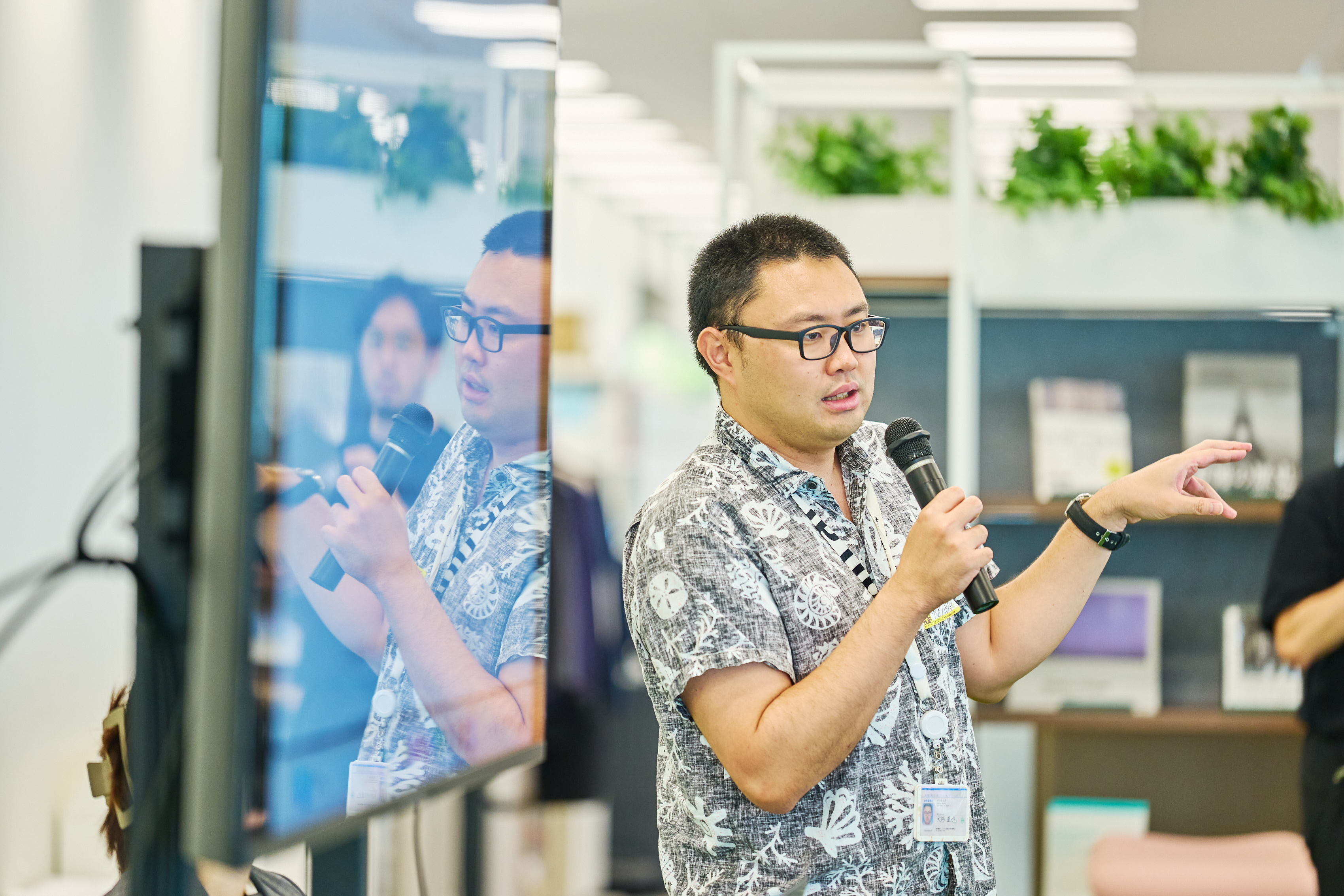 デジタル庁・大杉直也が登壇して話している写真。モニターの脇に立ち、右手でマイクを持って話している。
