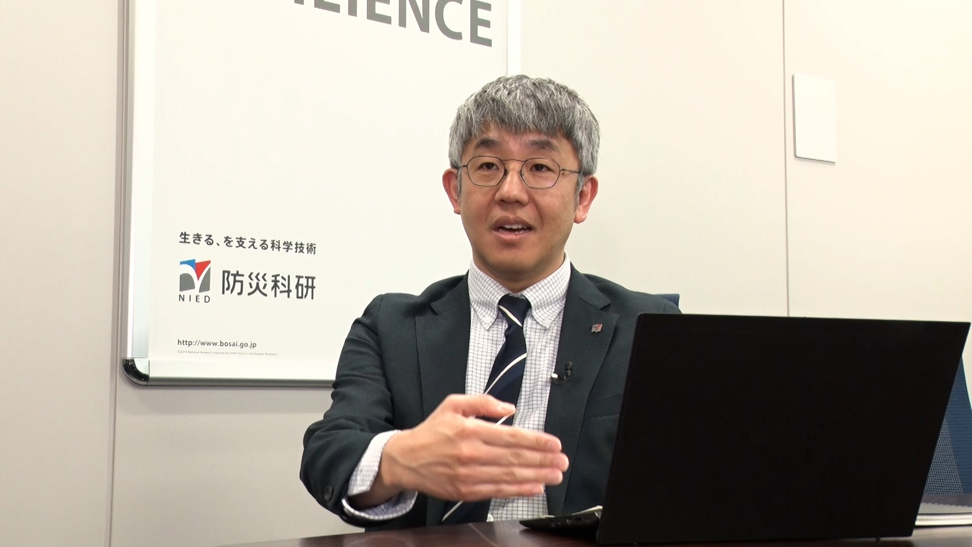 会議室の壁を背景に、着席して話す防災科研の田口氏を正面から撮影 (※所属・職名などは取材時のもの) 。