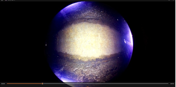球体型カメラ装置で管路内を撮影した映像のキャプチャ画像。黒い背景に円形に、ライトに照らされたコンクリート管の頂部（中央、白色箇所）と側面（上下、黒色箇所）の様子が映し出されている。下部に動画のシークバーが表示されている。