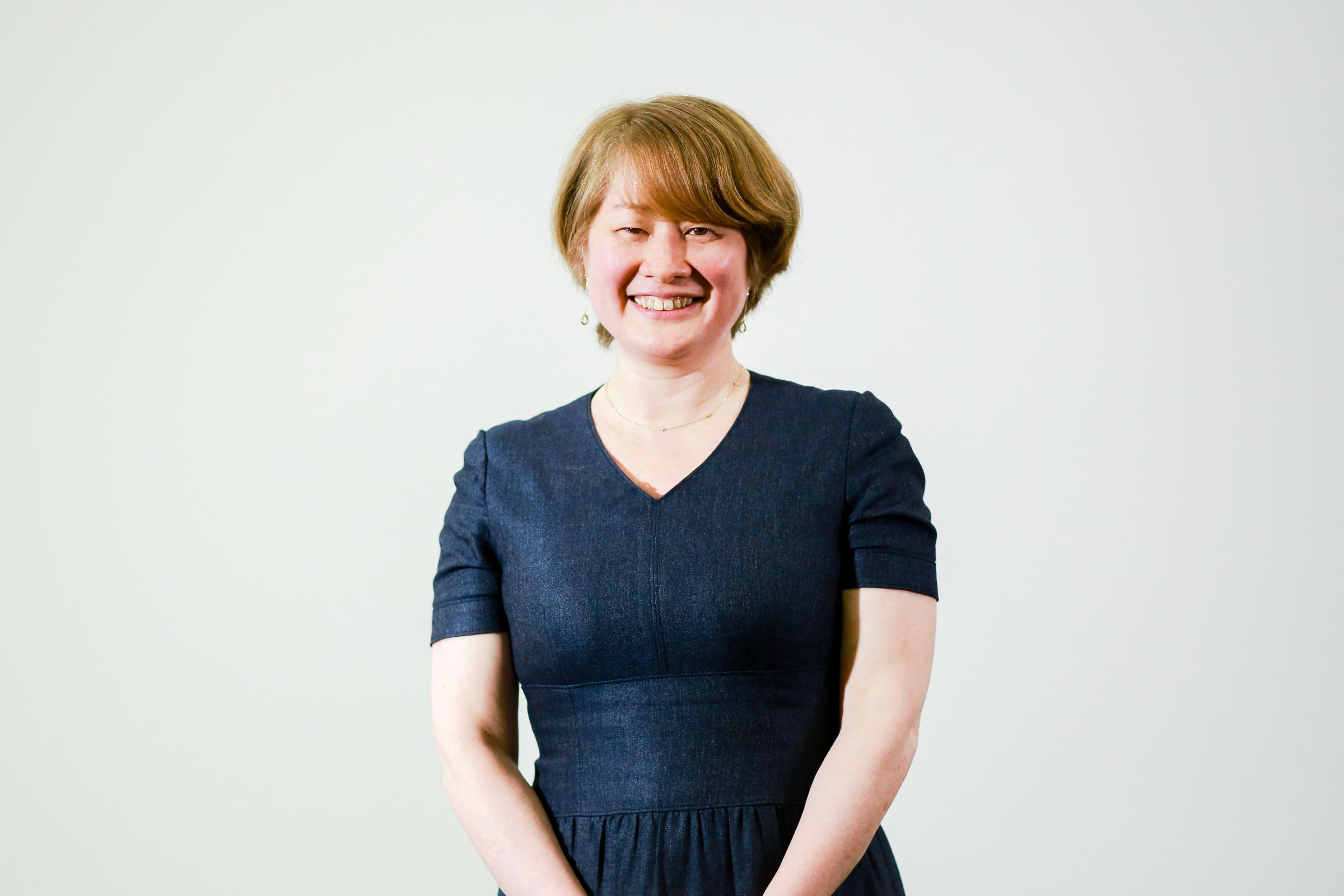 住田のウェストショット。白壁の背景で、正面を向いてにこやかな表情で立っている。