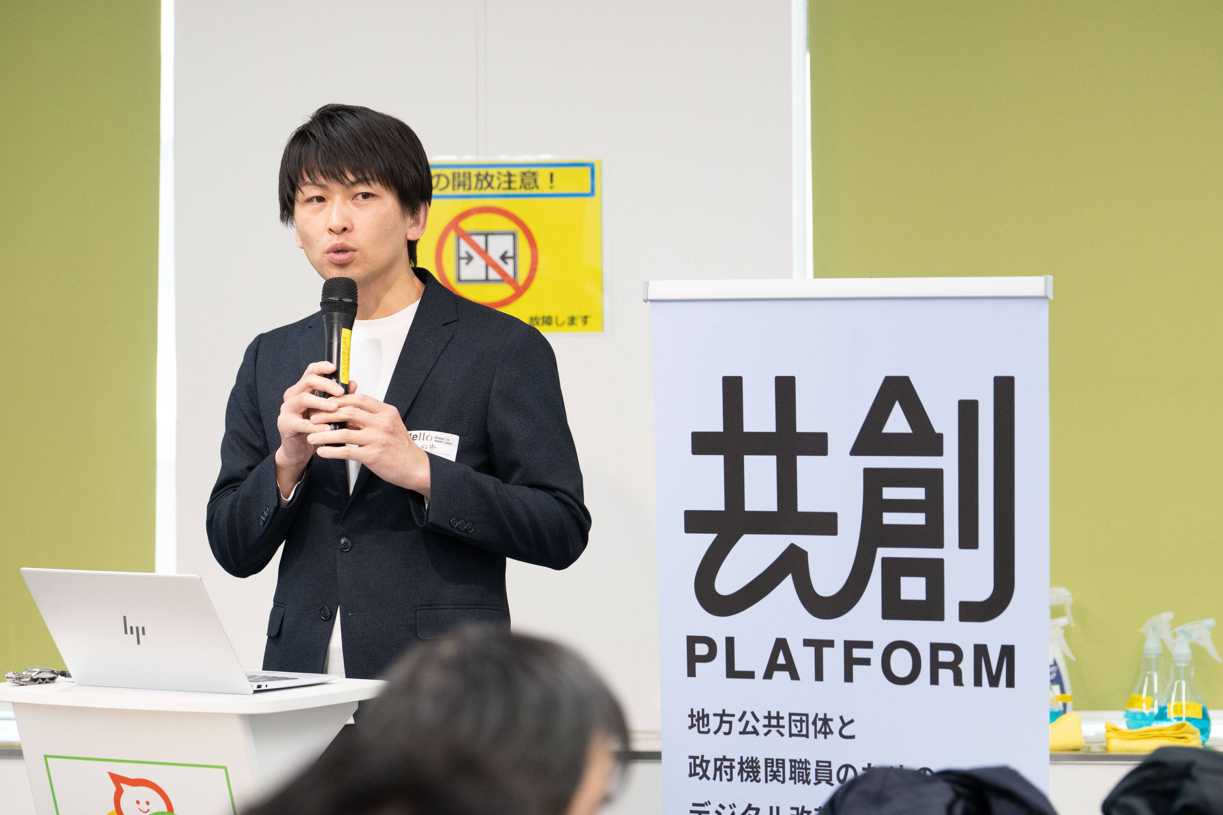 兵庫県三田市総務部DX推進課スマートシティ推進係の岩﨑謙二係長がマイクを持って登壇している様子。