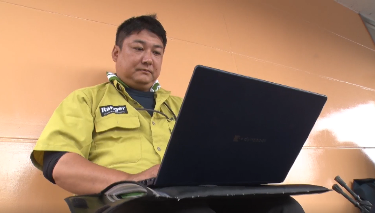 SIMが内蔵されているGSS端末のノートPCを使い、オフィス外でも仕事をする岡島所長が写っている写真。