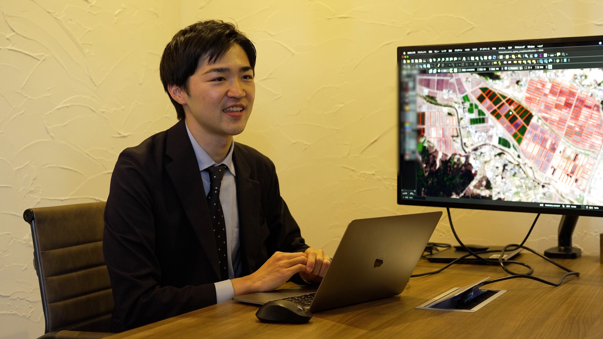 ノートパソコンが置かれた机に着席するLAND INSIGHT代表取締役副社長の遠藤氏のバストアップ写真。遠藤氏の右手には衛星画像を映したモニターが置かれている。