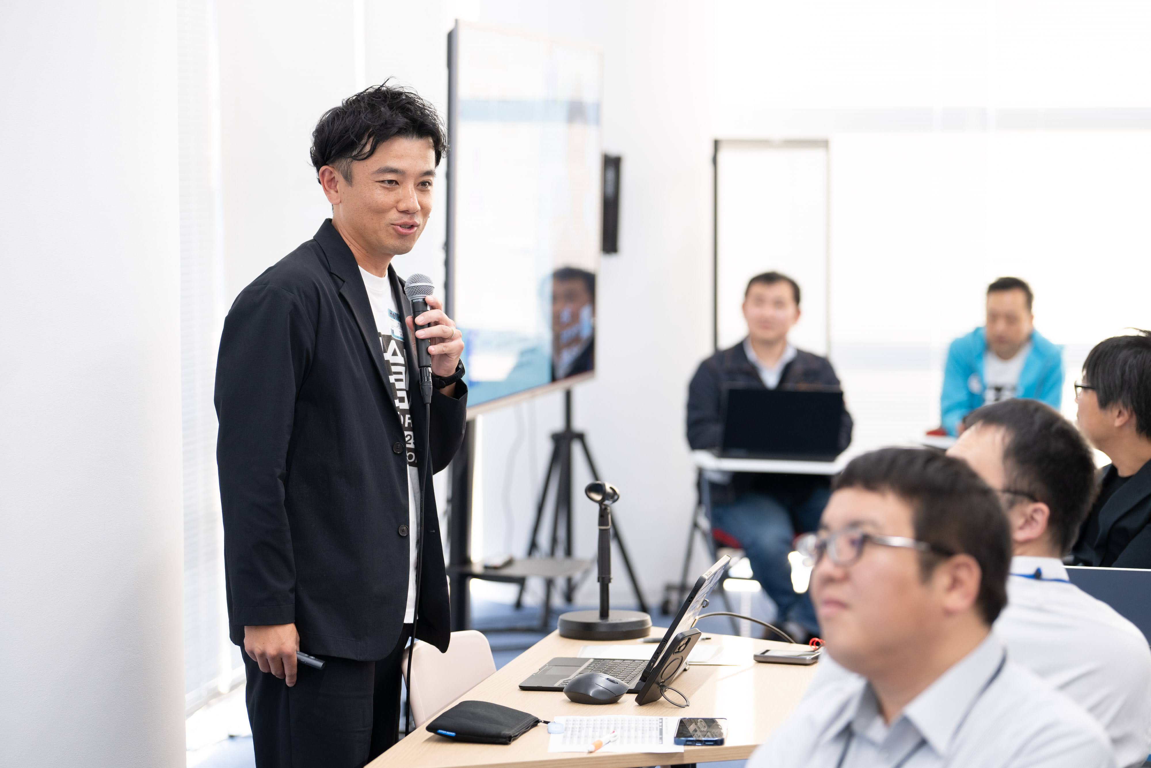 岐阜県下呂市の長尾飛鳥氏がマイクを持って、参加者に向かってプレゼンテーションをしている様子。