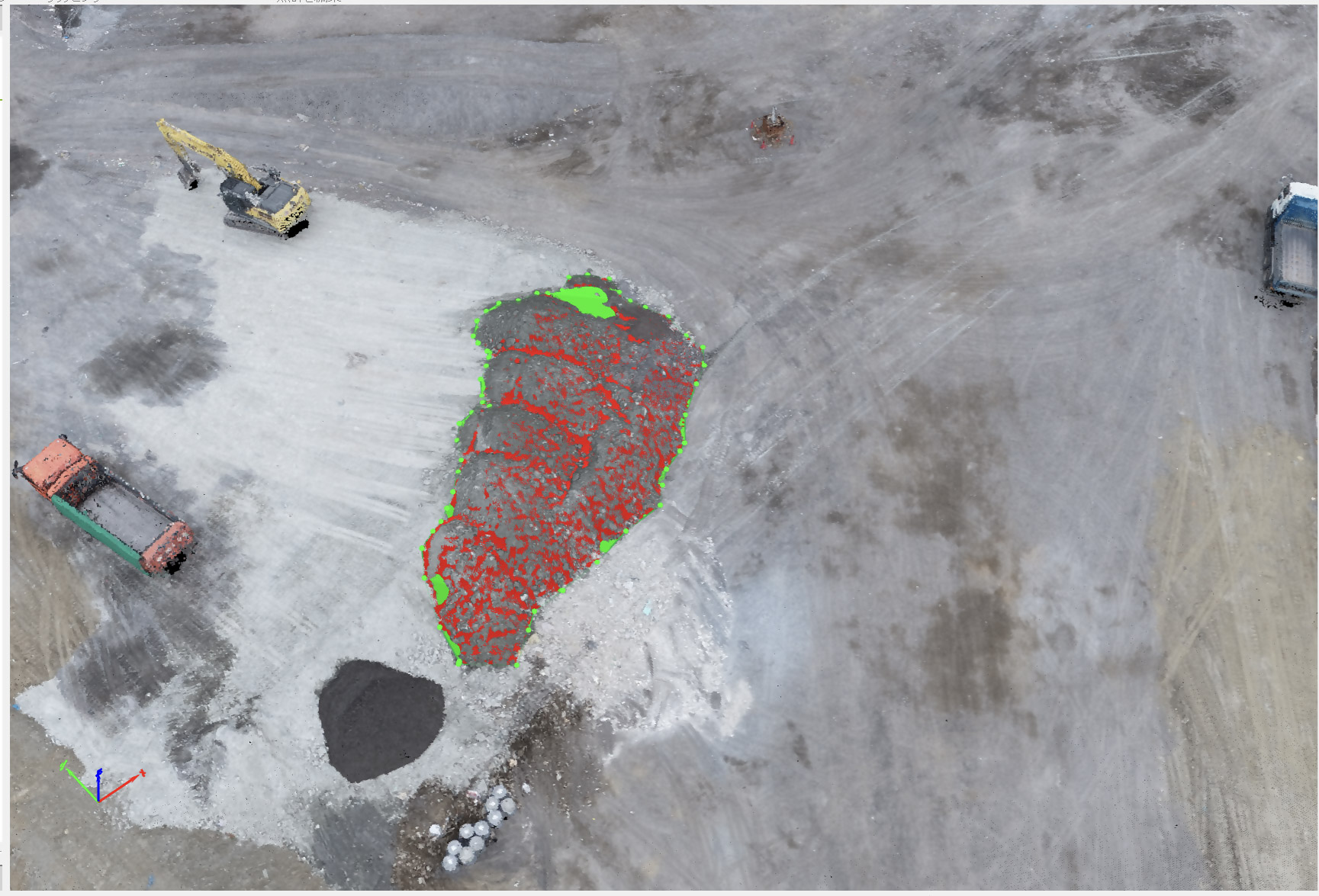 ドローンで撮影した産業廃棄物最終処分場の画像データ。画面中央に土砂の山があり、その輪郭と表面に赤色の点群と緑色の点群が重ねて表示されている。左にはショベルカー、左下にはダンプトラック、右上にも車両が確認できる。左下にはXYZ座標軸（青・緑・赤）が表示されている。
