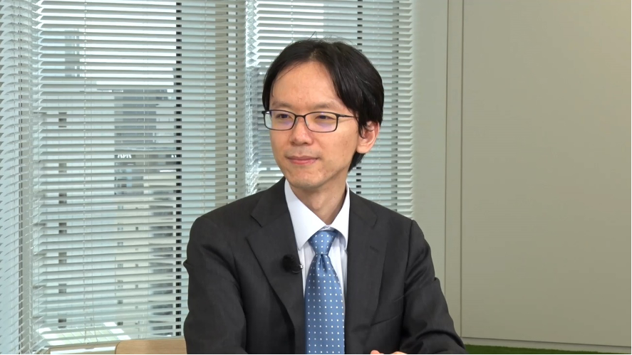 登 大遊氏のバストショット。グレーのスーツを着た登氏が、窓を背景に座っている。