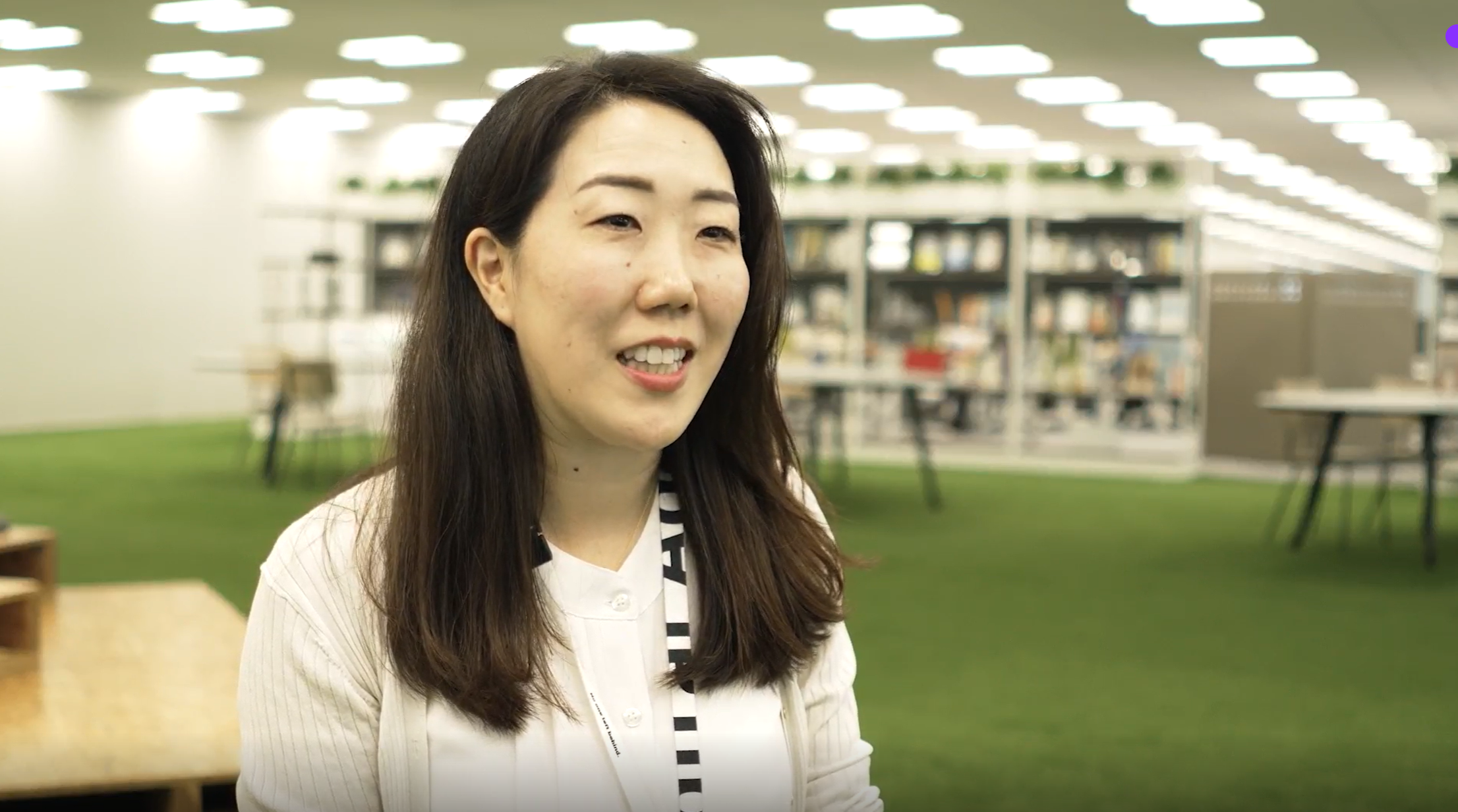 インタビューに応じるデジタル庁広報の石田のバストショット。芝生が敷かれたオフィスを背景に話をしている様子を、右斜め前から撮影している。