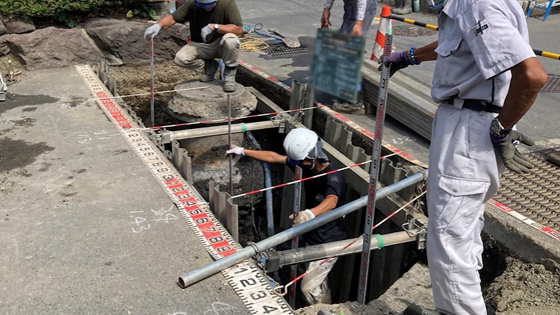 道路を掘り起こし、ガス管や水道管などの位置を人が測定し記録するアナログな作業の様子の写真