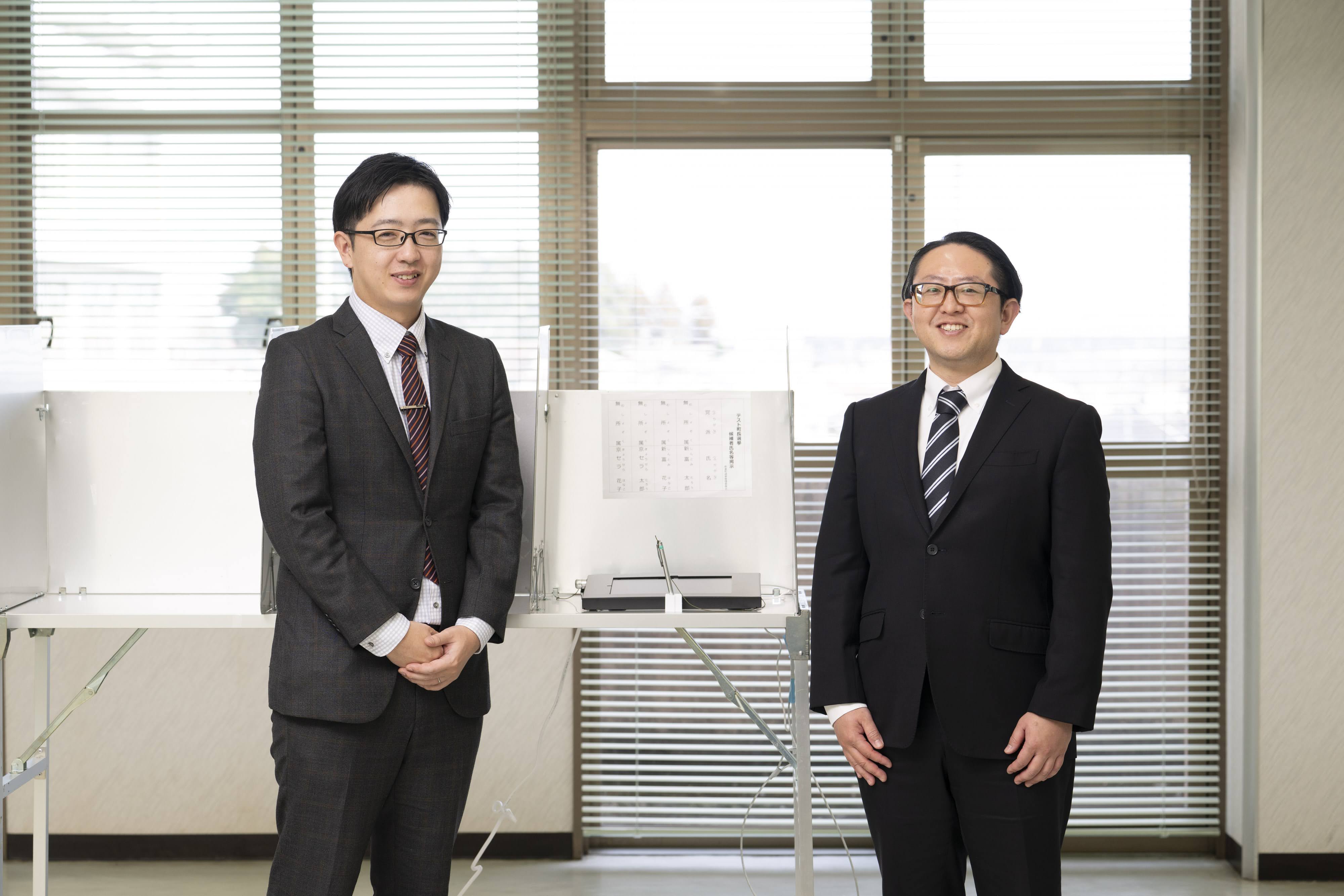 吉野主査（左）と甲斐係長が、タブレット端末が置かれた記載台を挟んで立っている。