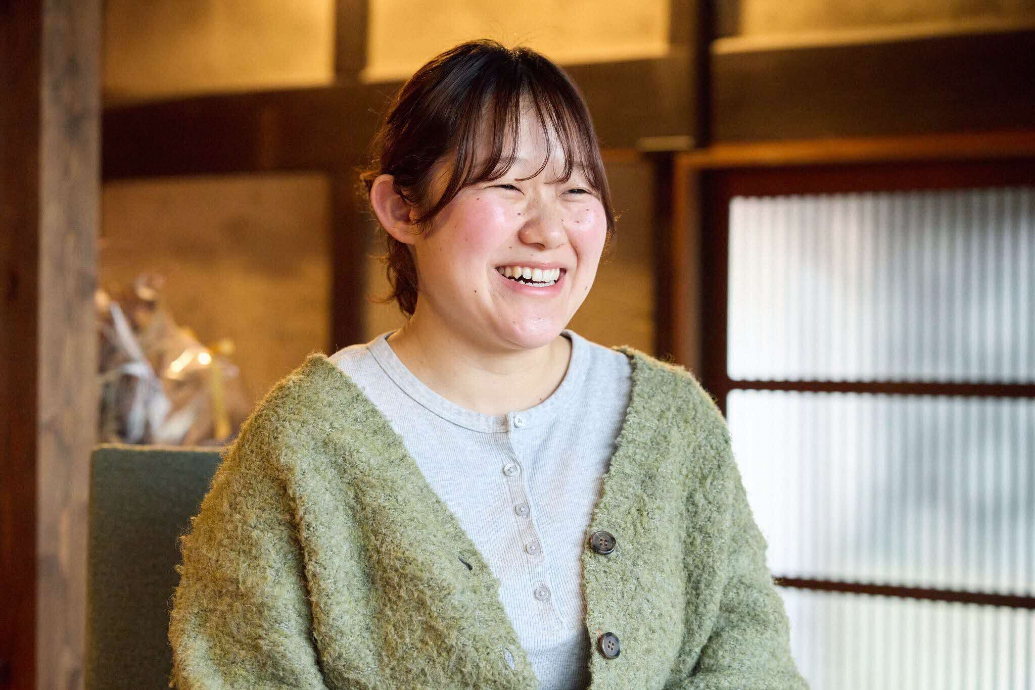 インタビューに応じる石川楓さん。背景は木材の柱や引き戸が見える和室で、温かみのある照明が空間全体を柔らかく照らしている。