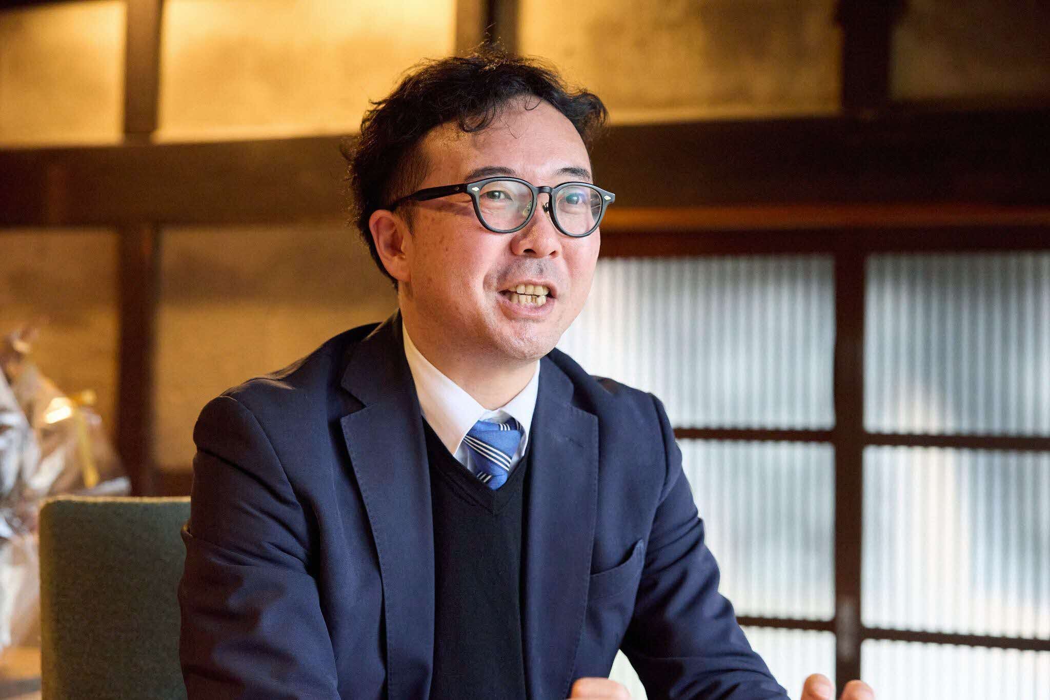 インタビューに応じる島根県の望月係長。背景は木材の柱や引き戸が見える和室で、温かみのある照明が空間全体を柔らかく照らしている。