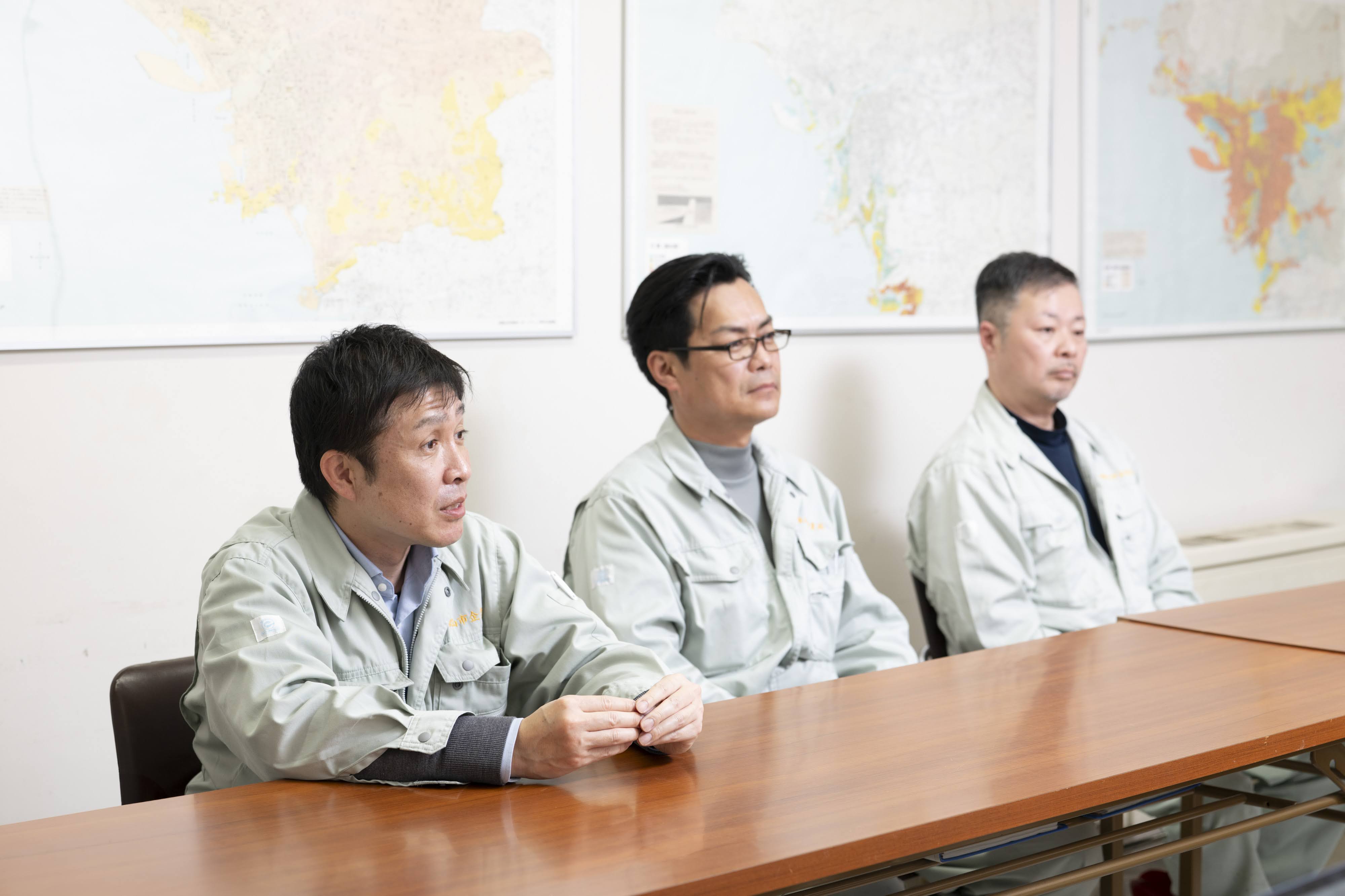 会議室の木製テーブルを前に、和歌山市職員が作業服姿で横並びで着席している。左端手前の男性が話している。背景の壁には大判の地図が複数枚掲示されている。