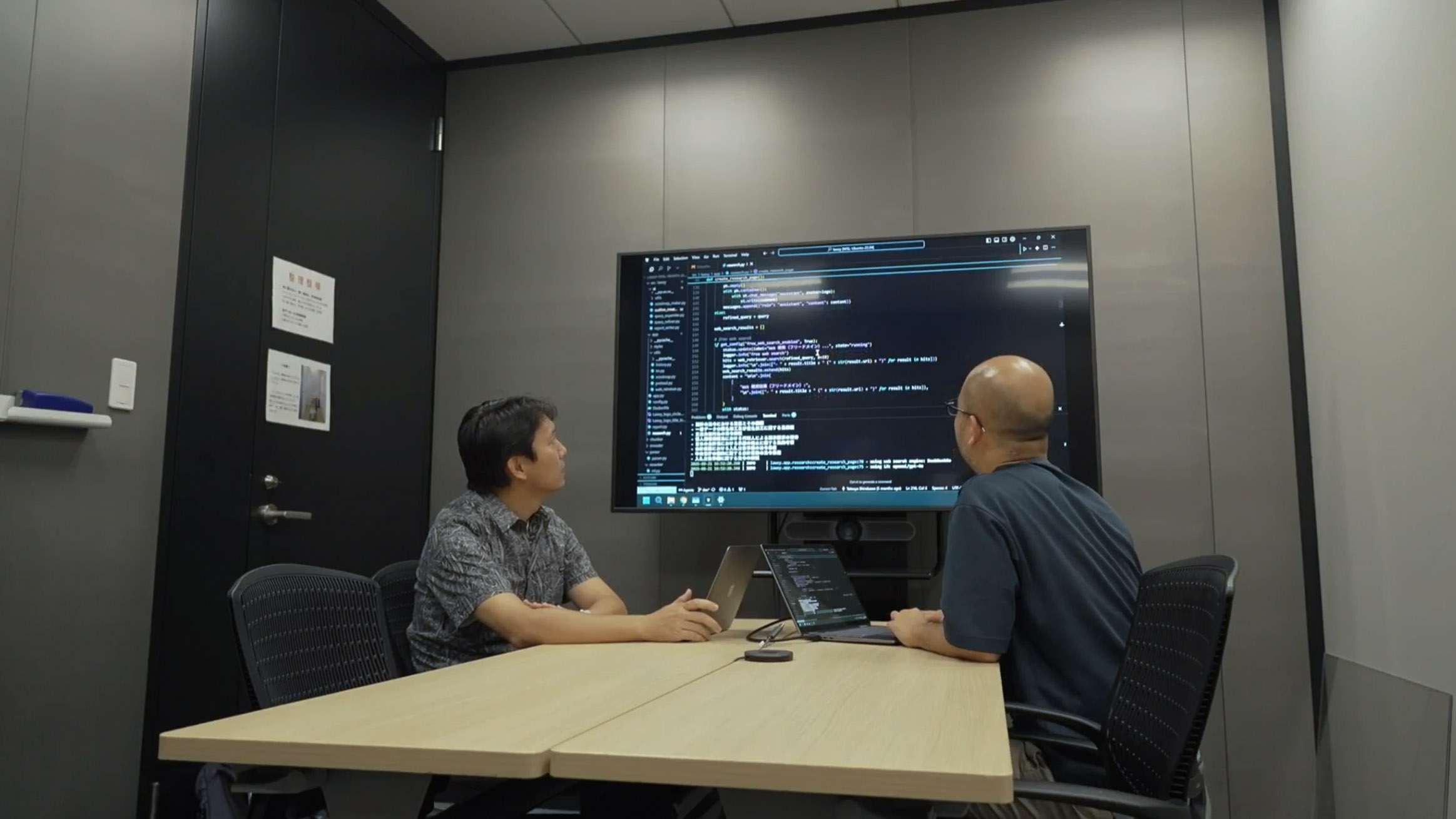 Lawsyの開発者二人がモニターを見ている写真。モニターには、AIアプリとして源内に導入された「Lawsy」の開発画面が投影されている。