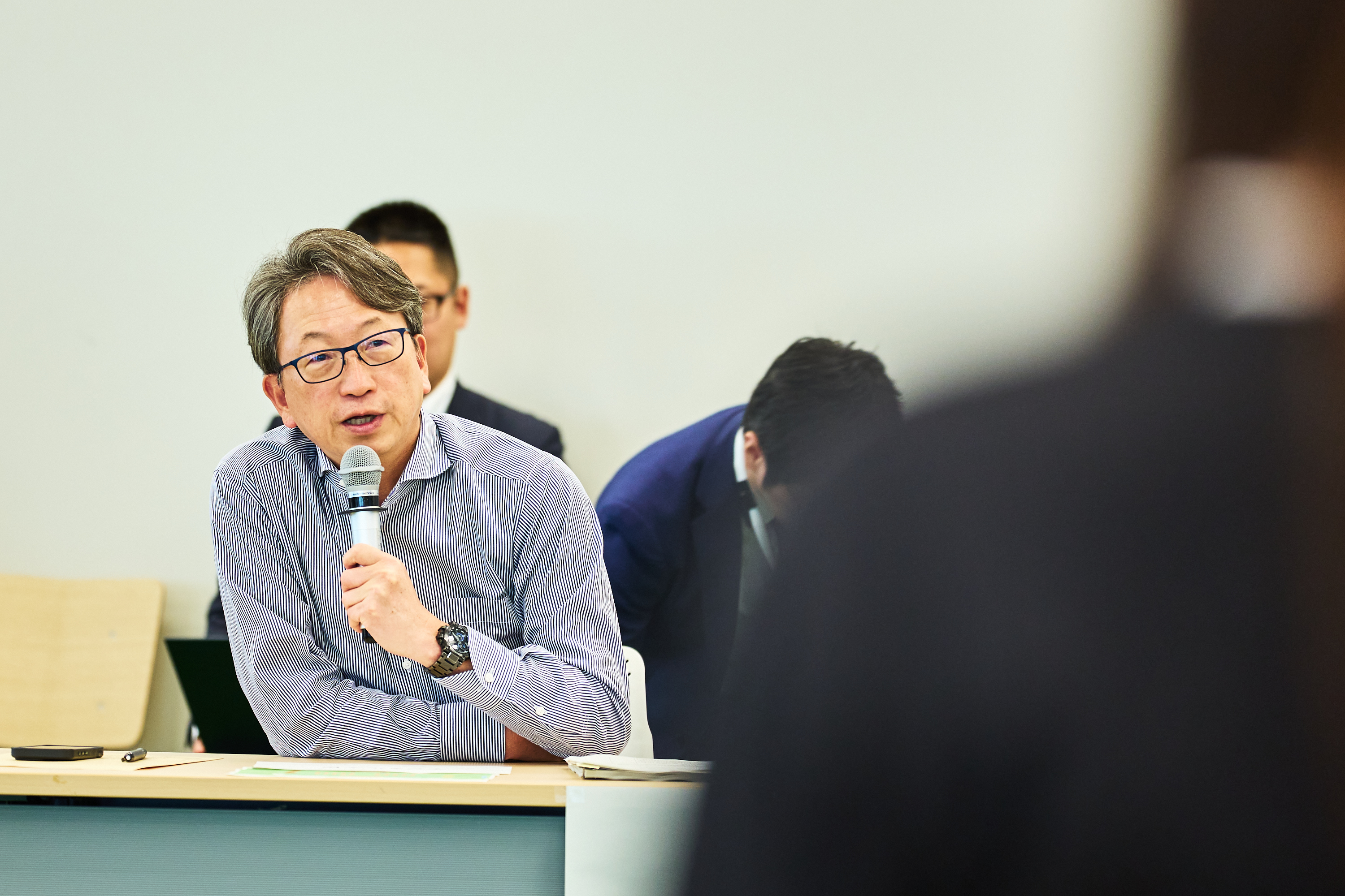 デジタルマーケットプレイス活用交流会で所感を述べる平デジタル大臣を正面から撮影。左手にマイクを持ち、着席した状態でコメントしている姿を、参加者の肩越しに撮影している。