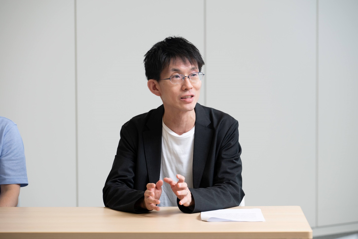 インタビューに応じる経済産業省の木村補佐の写真。オフィスで壁を背景に、椅子に座り、両手を机の上に置いて話している様子を正面から撮影している。