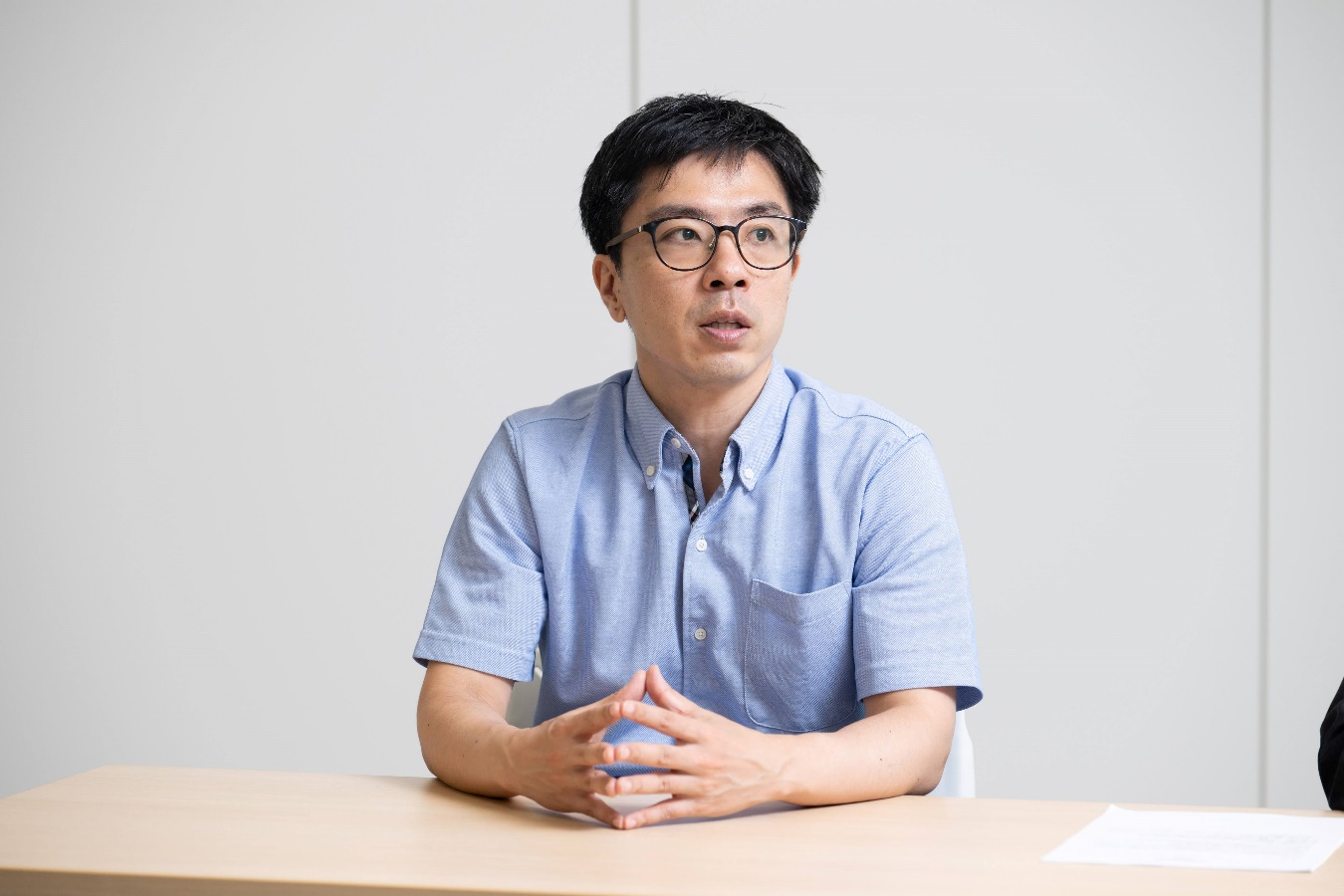 インタビューに応じるデジタル庁の黒籔参事官の写真。オフィスで壁を背景に、椅子に座り、両手を机の上に置いて話している様子を左斜め前から撮影している。