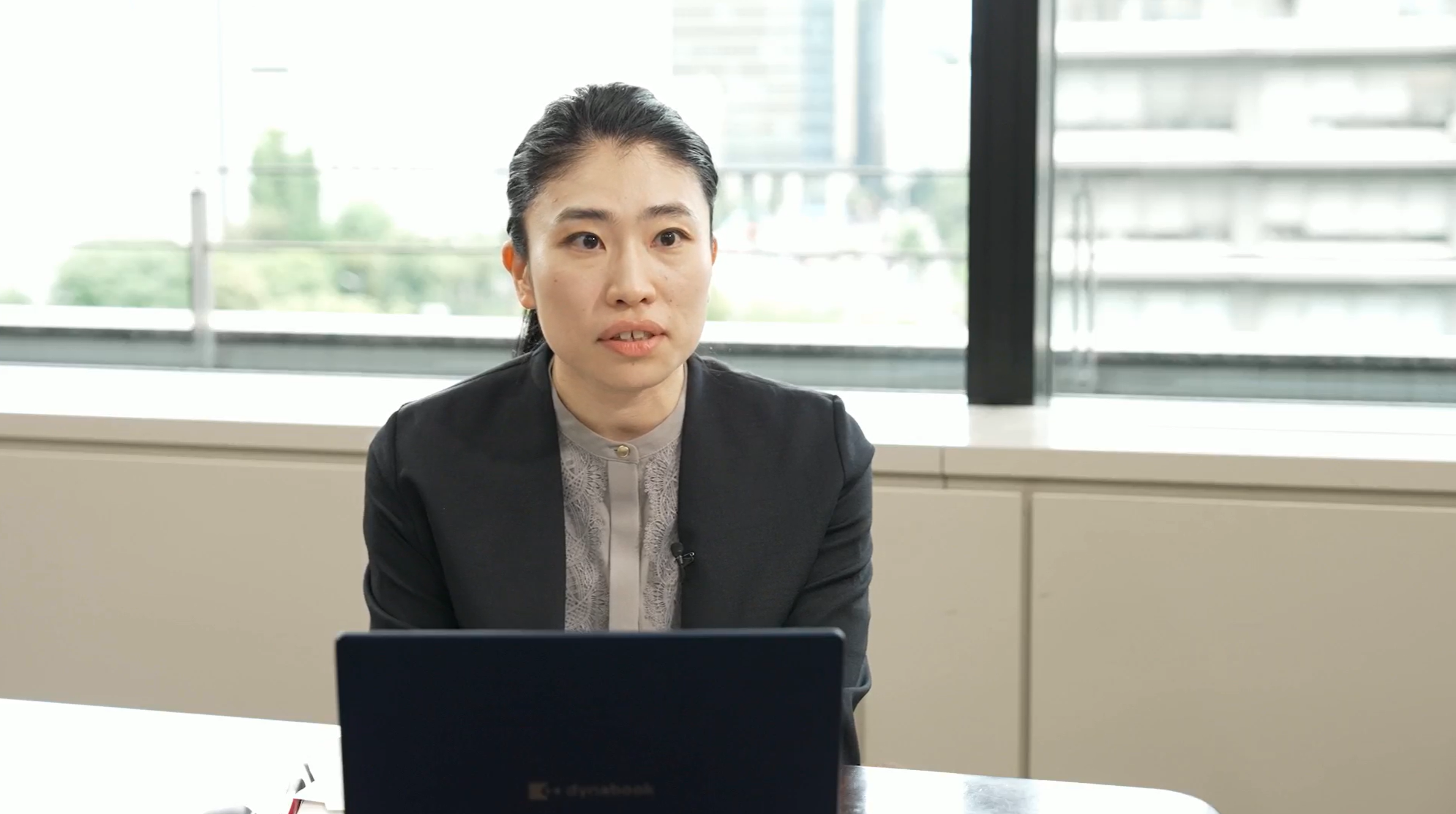 動画の切り取り画像。水道ダッシュボードの開発に携わった総務省自治財政局公営企業経営室の矢島夏美係長がインタビューに答えている様子。矢島係長の前にはパソコンがある。