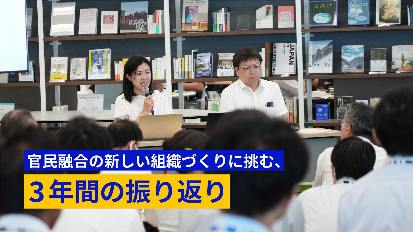 多くのデジタル庁職員が集まっている。司会者の女性と登壇者の眼鏡をかけた男性が写っている。左下に官民融合の新しい組織づくりに挑む、3年間の振り返り と書かれている。