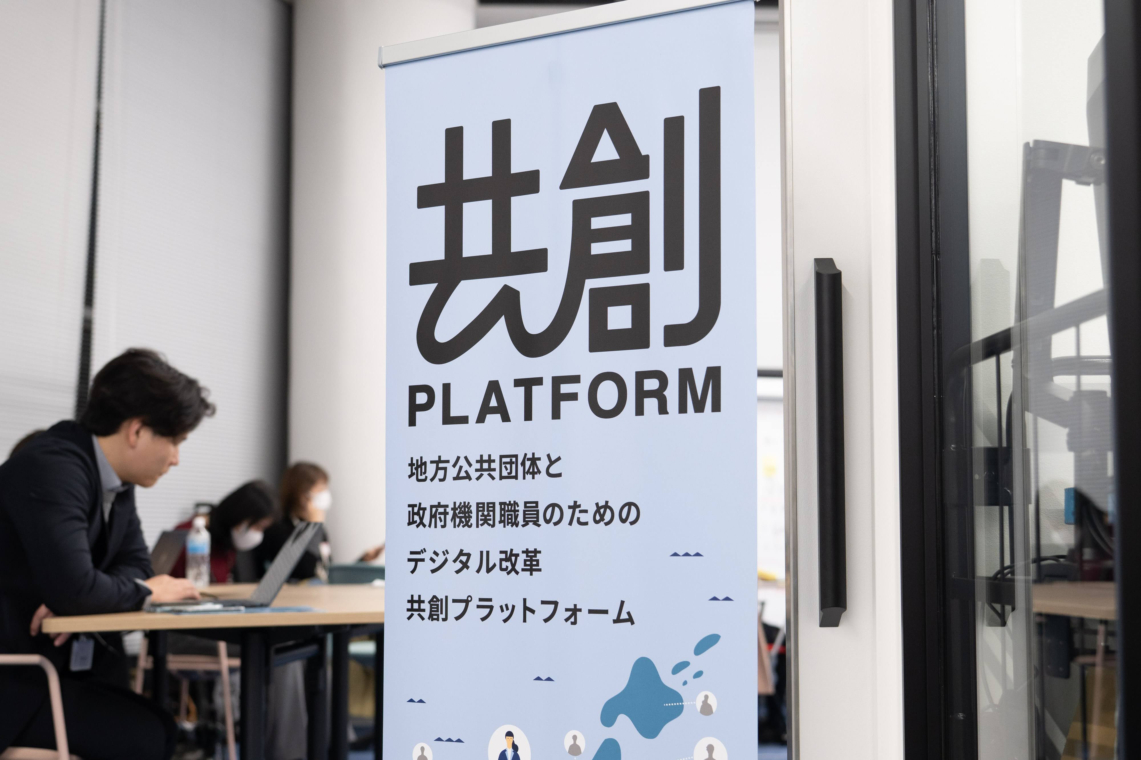 サムネイル写真。共創PFキャンプの会場の様子をうつしている。写真中央には「共創PLATFORM」と書かれた幟が置かれており、左側には着席してノートパソコンを操作する人物が写っている。