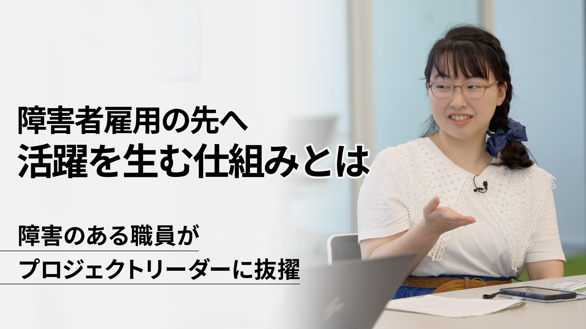 左側に大きく「障害者雇用の先へ 活躍を生む仕組みとは」とタイトルが表示され、その下に「障害のある職員が プロジェクトリーダーに抜擢」と記載されている。右側には、眼鏡をかけた若い女性がテーブルに座り、笑顔で手のひらを上に向けながら話している様子が写っている。