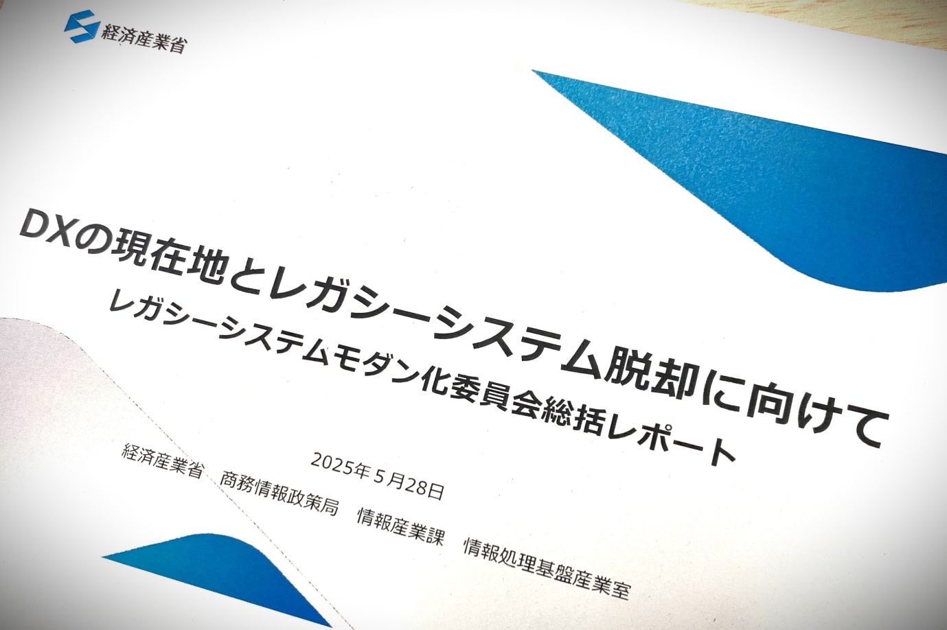 左上に「経済産業省」、真ん中に「DXの現在地とレガシーシステム脱却に向けて レガシーシステムモダン化委員会総括レポート」、その下に「2025年5月28日」「経済産業省　商務情報政策局　情報産業課　情報処理基盤産業室」と書かれた資料の表紙。