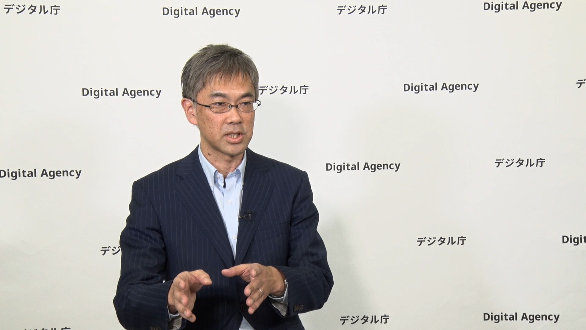 デジタル社会共通機能グループ 杦浦維勝参事官が、「デジタル庁」のロゴが入ったバックパネルの前で話す様子を正面から撮影 (※所属・職名などは取材時のもの) 。