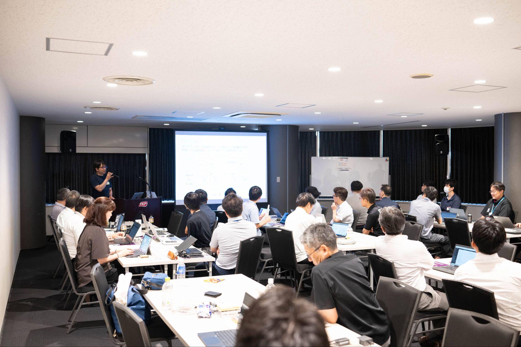 共創PFキャンプin広島 ガバメントクラウド編の様子。スクリーンに映し出された画面を参加者たちが眺めている。