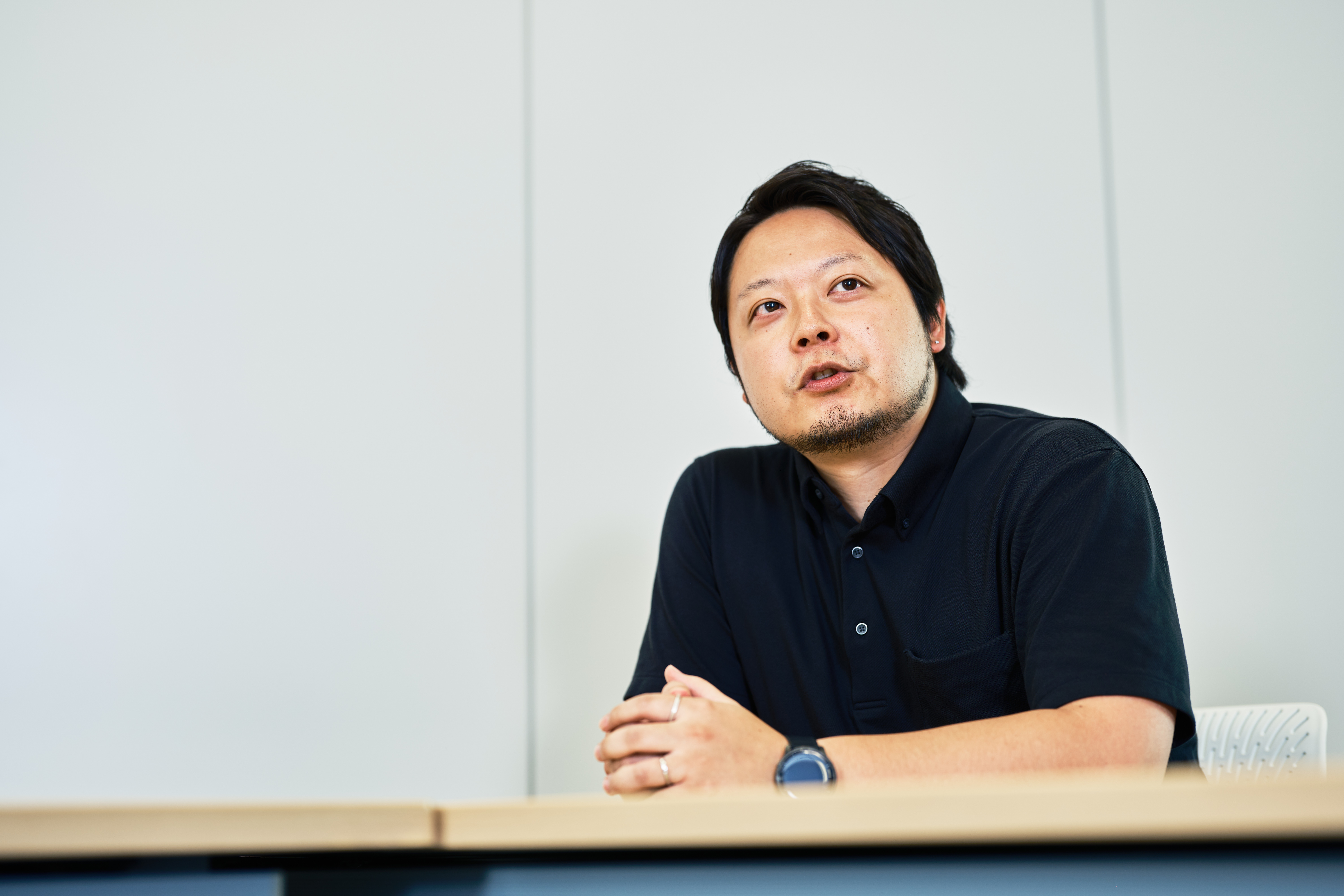 政策推進スペシャリストの松﨑が会議室の壁を背景に着席して話す様子と、向かって右手から撮影した写真。