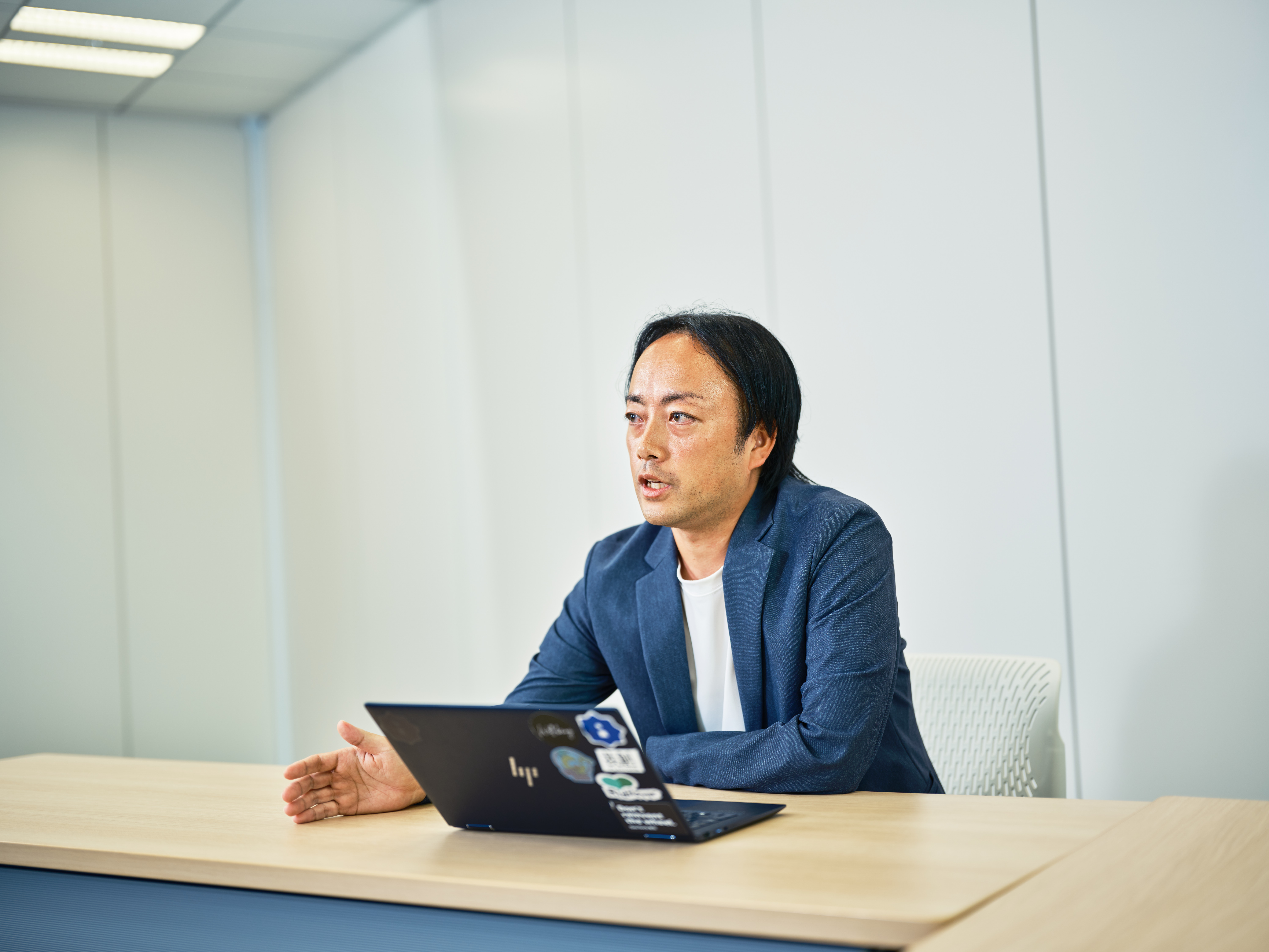 プロダクトオーナーの青野が椅子に座って、インタビューに応えている様子を向かって右手から撮影した写真。手元にはノートパソコンが置かれている。